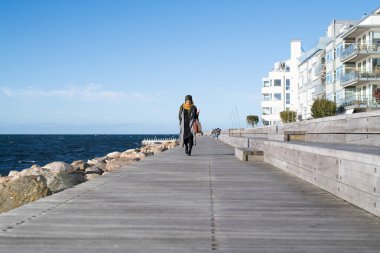 Başörtüsü takan kadın çantasıyla okyanusta yürüyor.