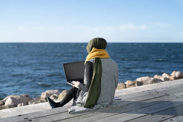 Başörtüsü Takan Genç Bir Kadın Dizüstü Bilgisayar Kullanarak Okyanusun Kenarında Telifsiz Stok Fotoğraflar