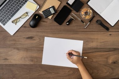 Sağ el, ofis ekipmanları ve iş aksesuarları ile boş kağıt üzerinde kalem tutuyor. Ofis masasının düz katmanında çalışıyor. Evrak işleri işi taklit ediliyor..