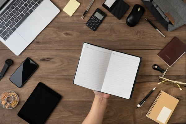 hand holding pencil on empty notebook list with office accessories on table flat lay.Working on office desk flat lay.To do list and Meeting reminder list on notebook concept.