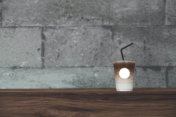 Ice Coffee on take away cup with Empty label for insert logo and graphic mockup template.Coffee cup on wood table and grunge concrete background.
