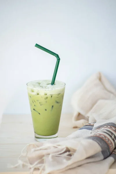 Teh hijau es atau matcha latte pada gelas tinggi dengan jerami di atas meja kayu putih dan dekorasi pakaian obyek . — Stok Foto