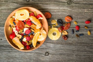 Mix of dried and candied fruit in bowl on a wooden background, top view clipart