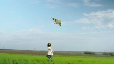 Neşeli küçük kız çalışır ve yeşil bir alanda bir uçurtma ile oynarken