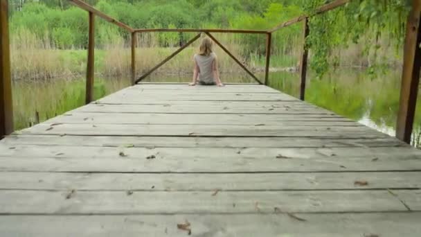 川の近くの木製の橋の上に座っている十代の少女 — ストック動画