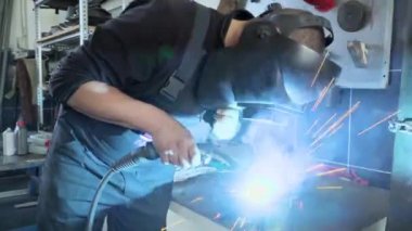 Bir atölyede kaynakçılık yapan maskeli yakın bir çalışan.