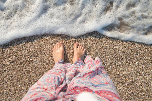 Bare feet of a girl on wet sand with a sea wave on the seashore