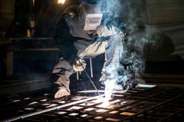 Bir atölyede kaynakçılık yapan maskeli bir işçi.