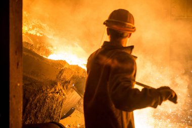 Kalıplardaki tanklardan sıvı metal dökerken çelik işçisi