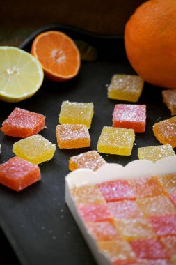 Siyah bir tepside, turuncu ve limonlu kesilmiş bir kutuda çok renkli turunçgil marmeladı.
