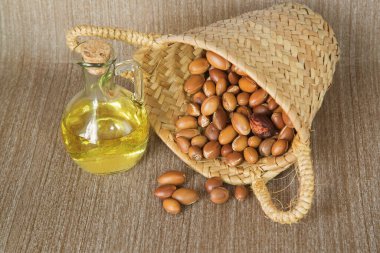 Hasır bir sepetin içinde cam bir yağ şişesiyle Argan fıstığı.