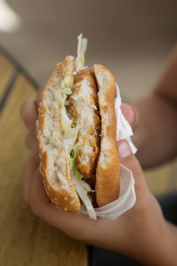 Ellerinde yarısı yenmiş tavuk burgeri. Zararlı beslenme kavramı