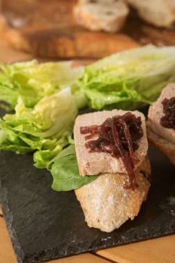 Karaciğer ezmeli bruschetta ve siyah tabakta soğan reçeli ve ahşap masa.