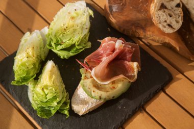 Jambonlu bruschetta (pastırma) ve siyah tabakta avokado. Güzel ve sağlıklı bir kahvaltı ya da atıştırmalık seçeneği