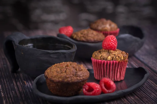 Rustik tarzda ahşap masada ahududu ve siyah kil çanak ile ev yapımı muffin