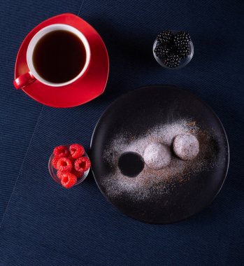 Ev yapımı çikolatalı kek topları truffels siyah plaka ve kırmızı ve siyah ahududu rustik tarzı koyu arka plan ile coffe fincan ile toz şeker serpilir.üst görünümü. Closeup.