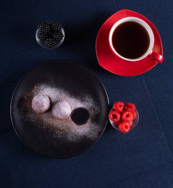 Ev yapımı çikolatalı kek topları truffels siyah plaka ve kırmızı ve siyah ahududu rustik tarzı koyu arka plan ile coffe fincan ile toz şeker serpilir.üst görünümü. Closeup.