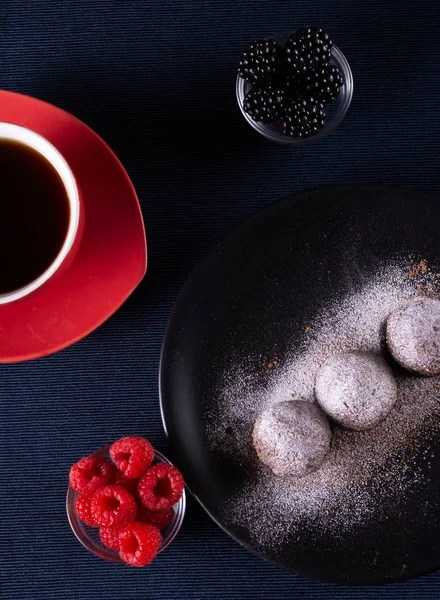 Ev yapımı çikolatalı kek topları truffels siyah plaka ve kırmızı ve siyah ahududu rustik tarzı koyu arka plan ile coffe fincan ile toz şeker serpilir.üst görünümü. Closeup.