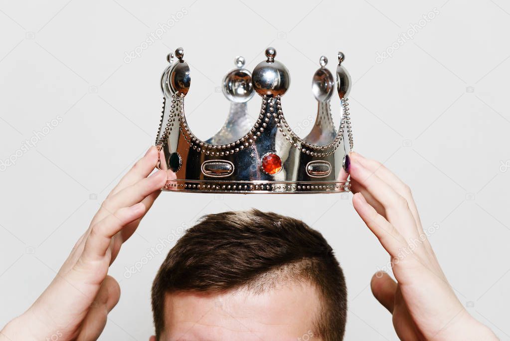 Coronation.  Dressing the crown on the head. Business concept - appointment manager. Man hands holding crown over his head, on light gray background, in studio.