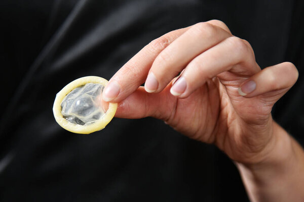 Презерватив в руке девушки на тёмном фоне. Сексуальные аксессуары вблизи.