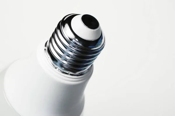 Enerji tasarrufu ekonomik ampulü yaktı. Beyaz arkaplanda lamba ipliği olan metal taban.