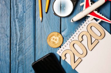 2020 ve kalem, ahşap bitcoin, akıllı telefon ve mavi ahşap masa üstünde oyuncak bir uçağın maketini içeren defter..
