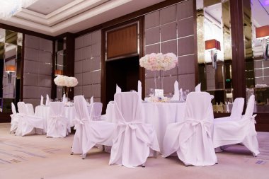 Restoranın yemek salonu beyaz masa örtüleri ve çiçeklerle dolu.