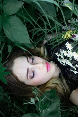 Gotik tarzında bir buket kurumuş çiçekle çimlerin üzerinde duran bir kızın portresi..