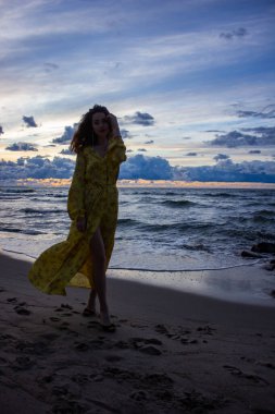 Rusya, Kalininingrad bölgesi, Baltık Denizi, kız silueti alacakaranlıkta uzun sarı bir elbiseyle.