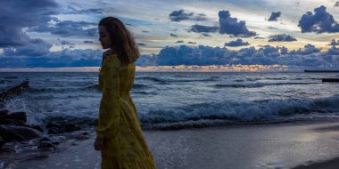 Rusya, Kalininingrad bölgesi, Baltık Denizi, kız silueti alacakaranlıkta uzun sarı bir elbiseyle.