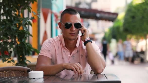 Young man talking by smartphone sitting at the outdoor cafe — Stock Video