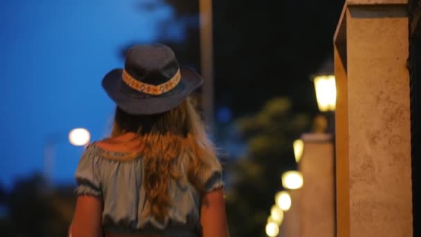 Молодая женщина в шляпе уходит на ночную улицу города — стоковое видео