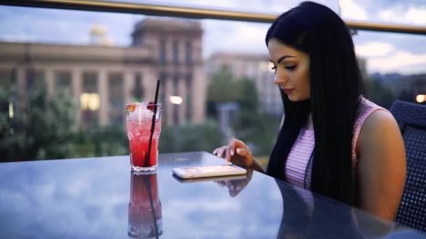 Mujer bebiendo cóctel frío fresco mirando hacia abajo a teléfono inteligente — Vídeos de Stock