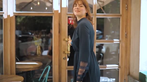 Женщина в платье, как швейцар, открывает дверь и приглашает в кафе — стоковое видео
