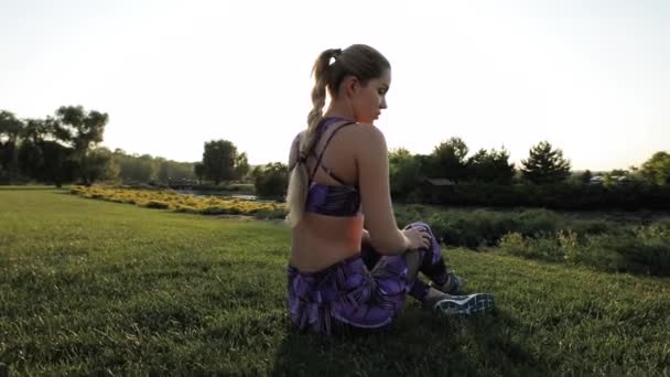 Femme sportive assise sur une pelouse en plein air, éruption de soleil — Video