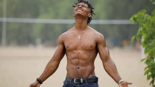 Сексуальный мужчина с мускулистым телом, стоящий под летним дождем с поднятыми руками — стоковое видео
