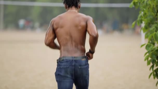 Hombre sexy con cuerpo muscular corriendo en la playa bajo la lluvia — Vídeo de stock