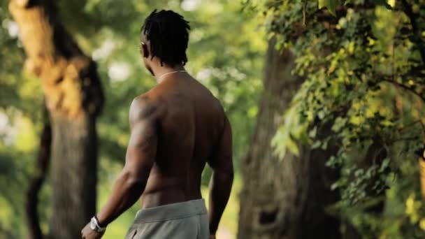Gespierde zwarte Afrikaanse man bodybuilder topless wandelen in een park — Stockvideo