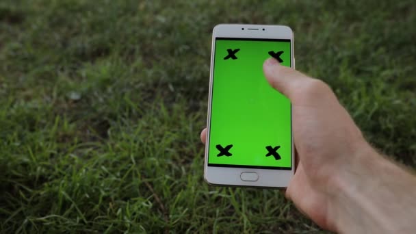 Çimenlerin üzerinde oturan smartphone yeşil ekran tutan erkek el — Stok video