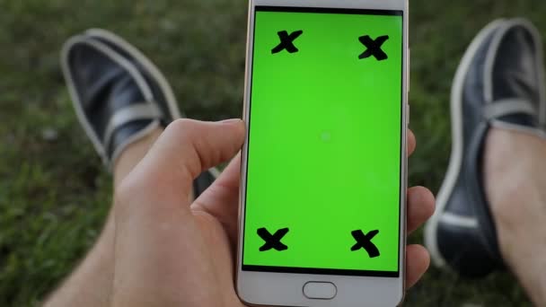 Male hand holding smartphone green screen sitting on grass — Stock Video