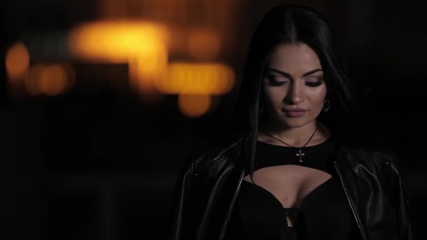 Mujer morena bonita en una ciudad nocturna envuelta en chaqueta — Vídeo de stock