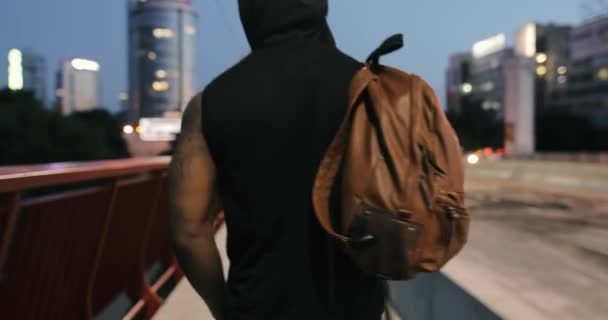 Man walking and thinking on a bridge in evening, holding bag, back view — Stock Video