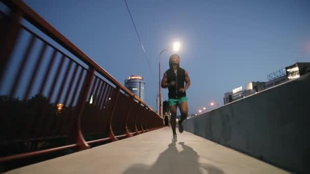 Hombre corriendo en un puente en la ciudad por la noche — Vídeos de Stock