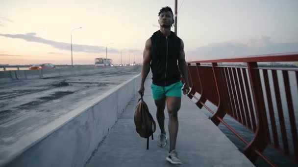 Hombre caminando y pensando en un puente por la noche, sosteniendo bolsa — Vídeo de stock