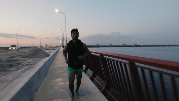 Hombre corriendo en un puente en la ciudad por la noche — Vídeo de stock