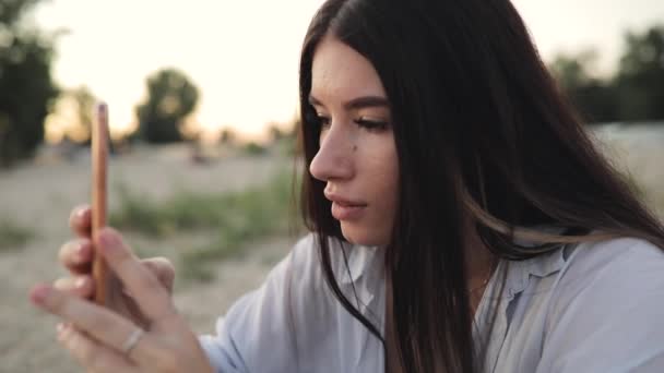 Vrouw met behulp van de smartphone zit filmen rivier strand — Stockvideo