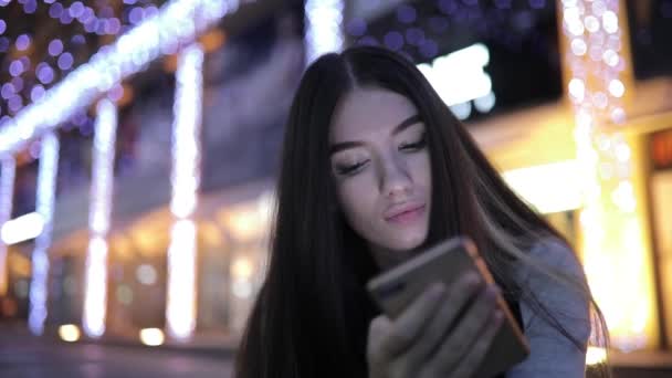 Женщина использует смартфон, сидя в центре города ночью — стоковое видео