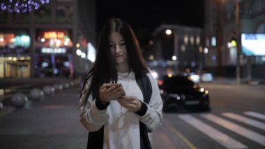 Gece şehir kullanma smartphone şehir merkezinde müzik dinlemek, yürüyen kadın