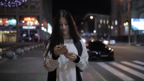 Vrouw lopen's nacht stad gebruik smartphone luisteren naar muziek in het centrum — Stockvideo