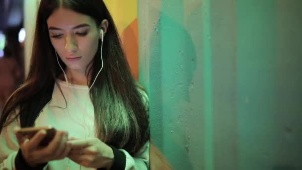 女性の夜の街で壁でリラックスして音楽を聴く — ストック動画